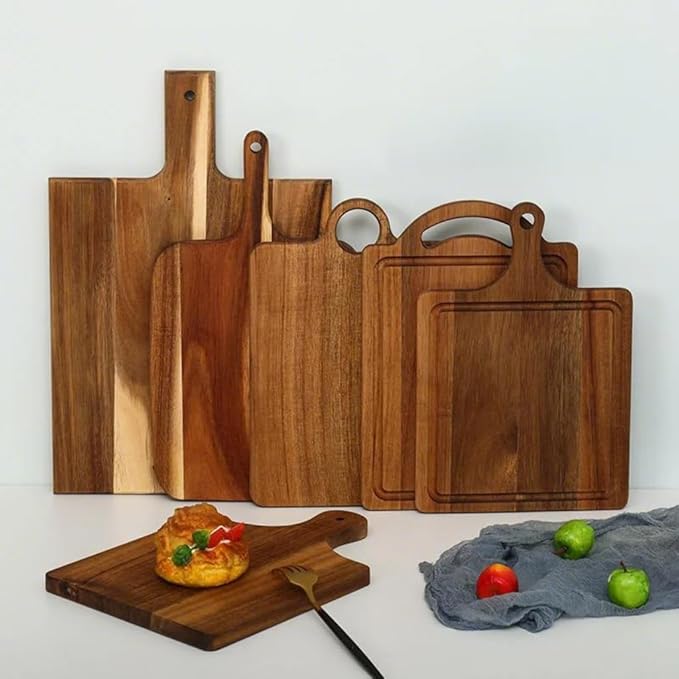 Set of wooden cutting boards in different sizes arranged against a light background; a small pastry rests on one board with a fork nearby.