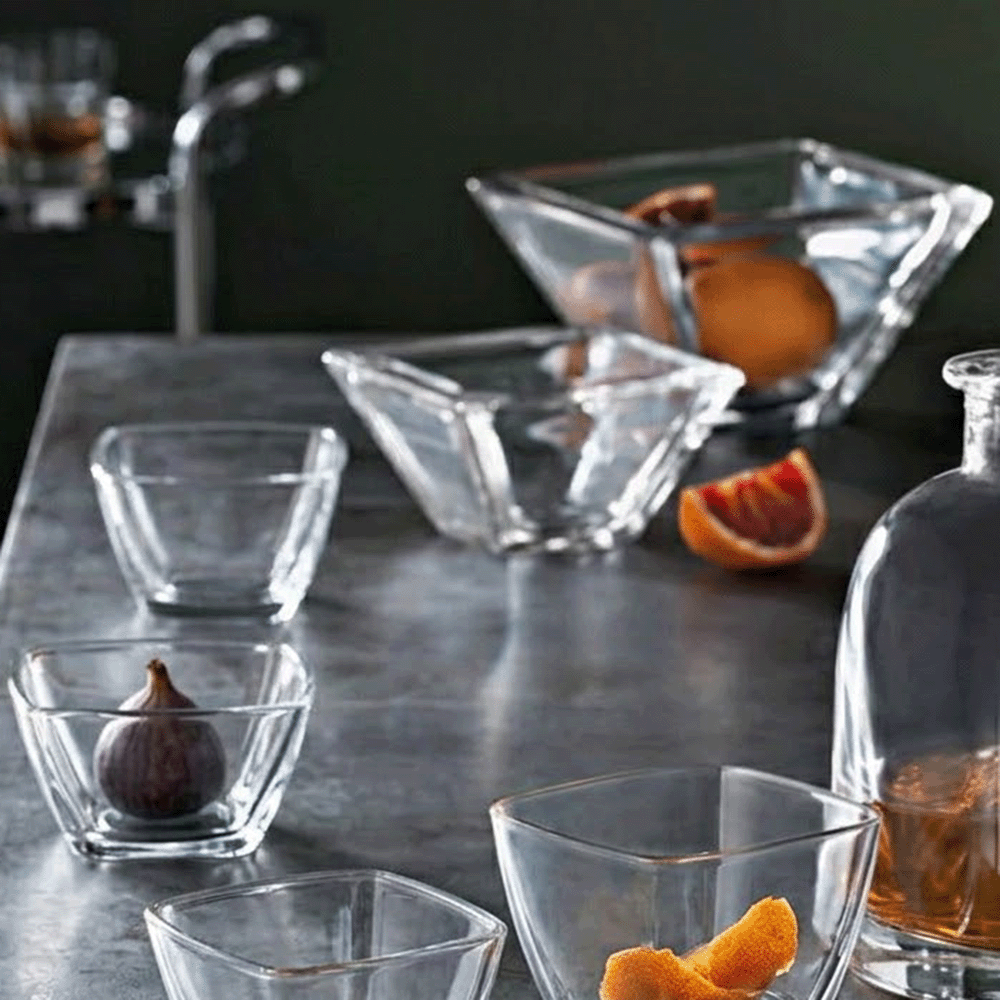 Assorted clear glass bowls and a bottle of amber liquor on a dark bar counter, with orange wedges and a fig inside bowls.