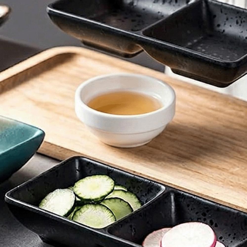 White ceramic cup of tea on a wooden tray with black serving dishes containing cucumber slices and radishes nearby.