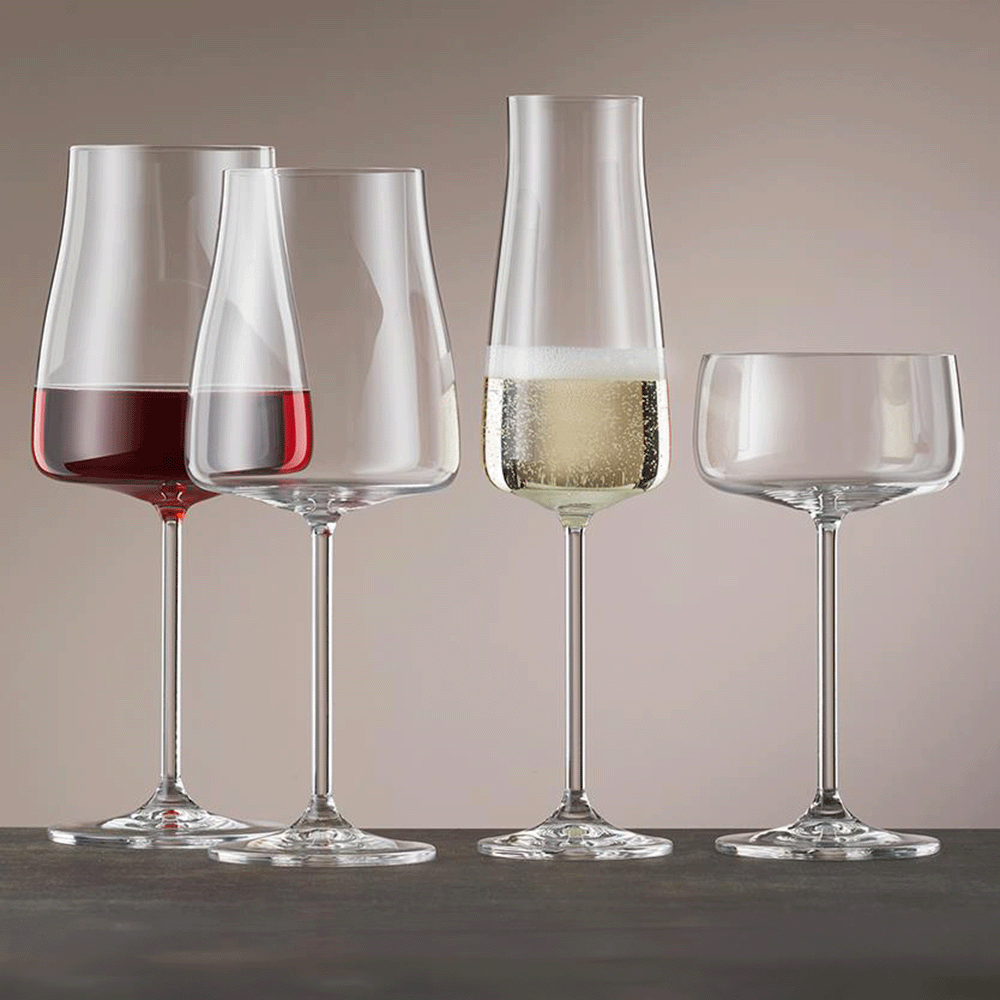 Four stemmed wine glasses in a row: leftmost contains red wine, second is empty, third holds sparkling white wine, rightmost is empty.
