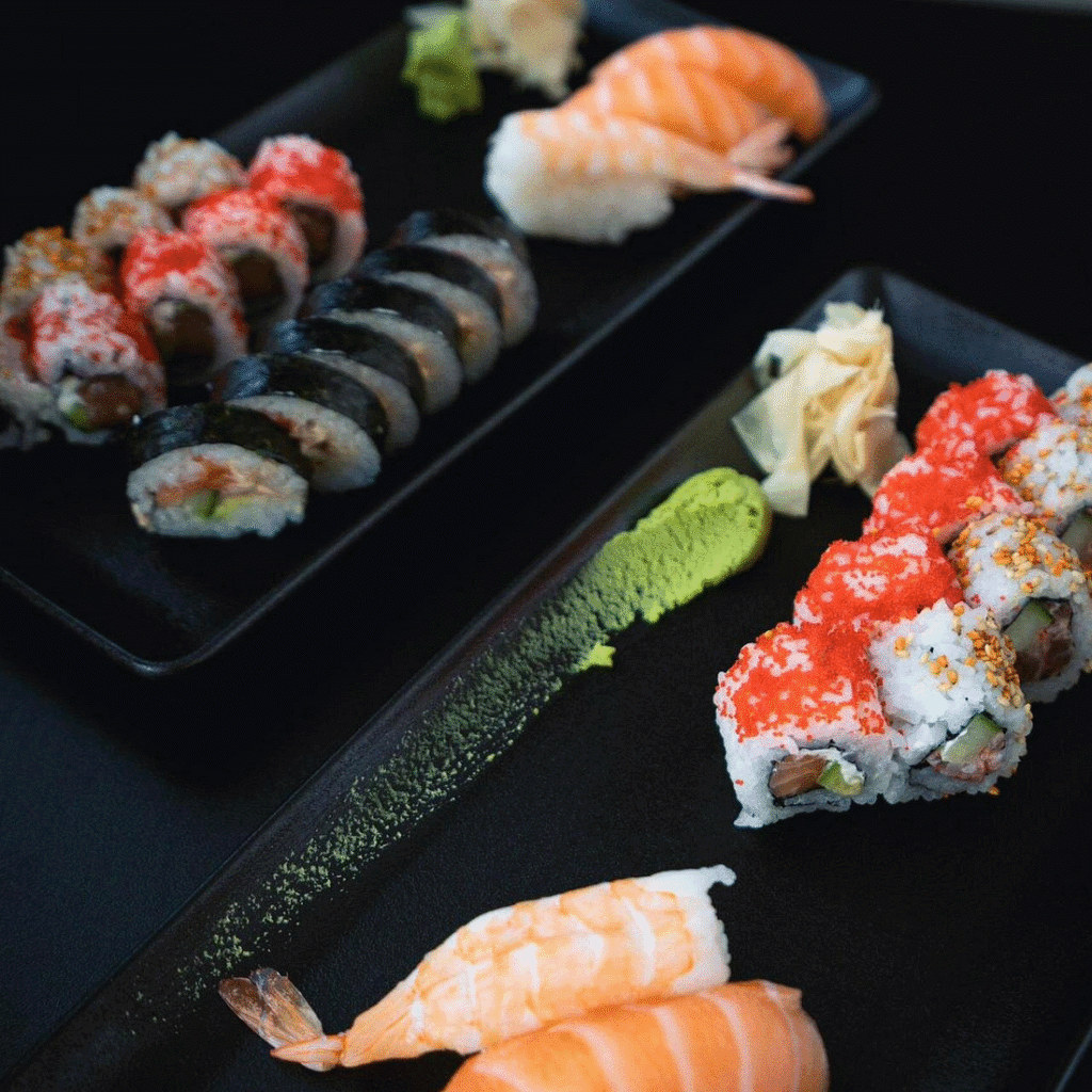 Assorted sushi platter with nigiri and maki rolls, wasabi, and pickled ginger on dark plates