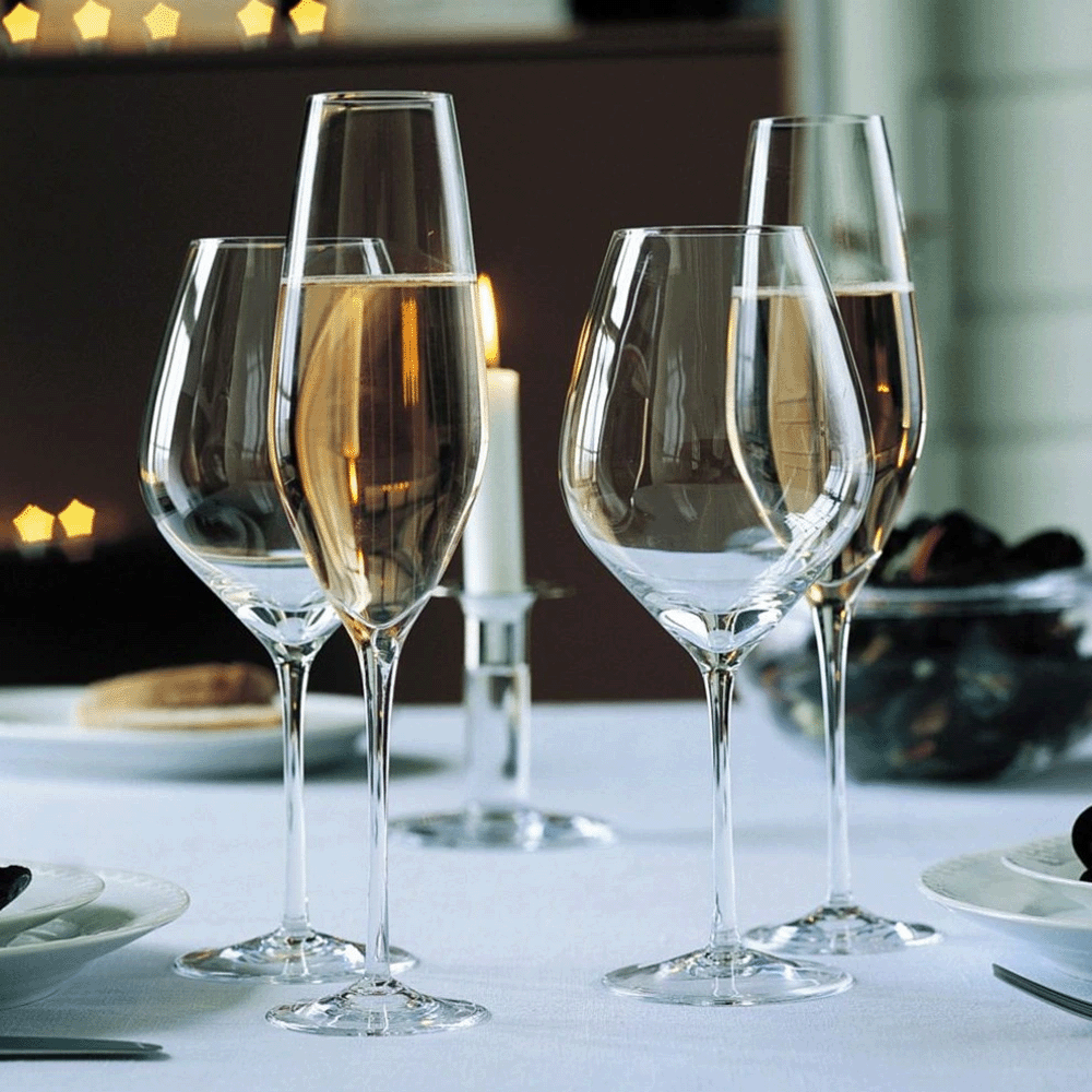 Several tall champagne flutes on a white tablecloth, candlelight glowing in the background for an elegant dinner setting.