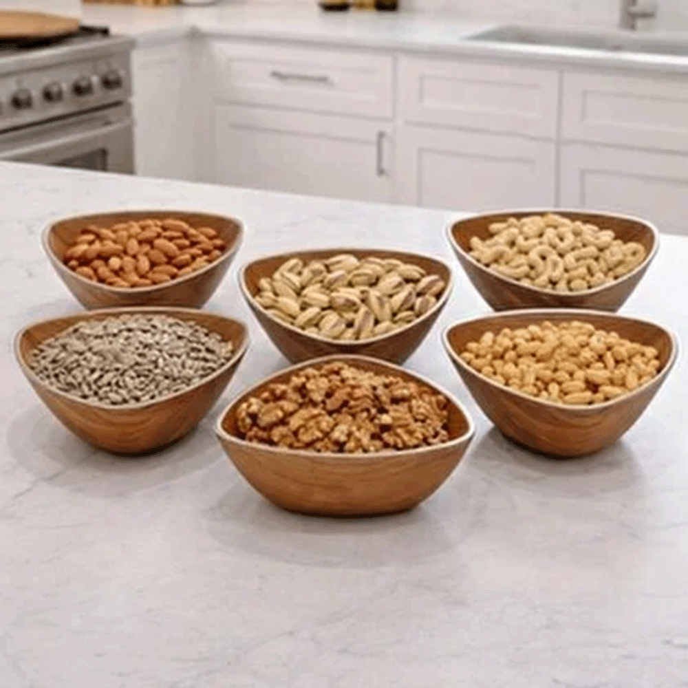 Six wooden bowls arranged on a white kitchen island, each filled with different nuts and seeds (almonds, pistachios, cashews, walnuts and mixed nuts).