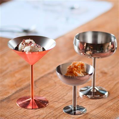 Three stemmed cocktail glasses on a wooden table, each with a frosty dessert or cocktail topped with whipped cream and crumbs.