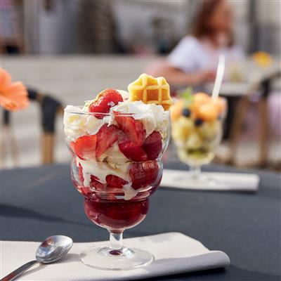 Parfait glass layered with strawberries, whipped cream, and waffle pieces on an outdoor cafe table.