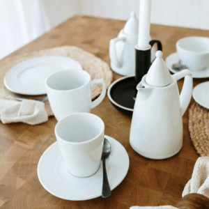 White ceramic teapot, cups, saucers, and plates arranged on a wooden table for a tea setting.