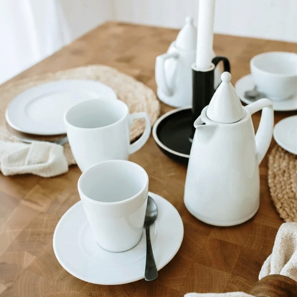 White ceramic teapot, cups, saucers, and plates arranged on a wooden table for a tea setting.