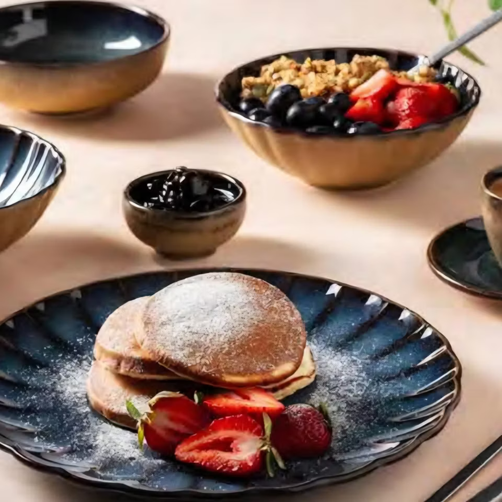 Blue plate with powdered-sugar pancakes, strawberry halves, and berries on a breakfast table.
