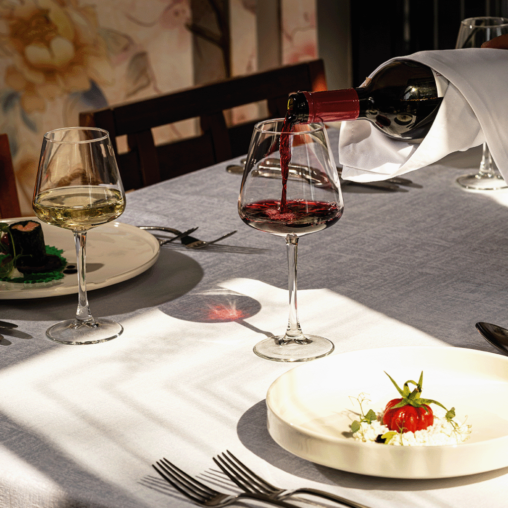 Wine is being poured from a bottle into a glass at an elegant dining table, with a plated dish nearby.